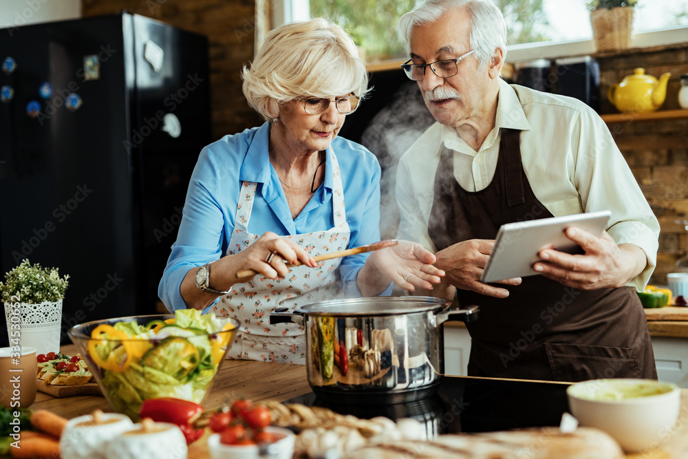 Senior couple cooking while following recipe on touchpad in the kitchen.