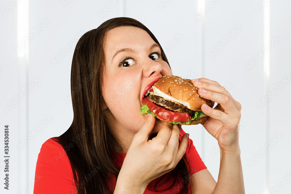 Young fat woman holds hamburger, smiles with opened mouth