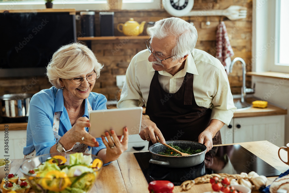 Happy mature couple having fun while using touchpad and cooking in the kitchen. Happy mature couple having fun while using touchpad and cooking in the kitchen.
