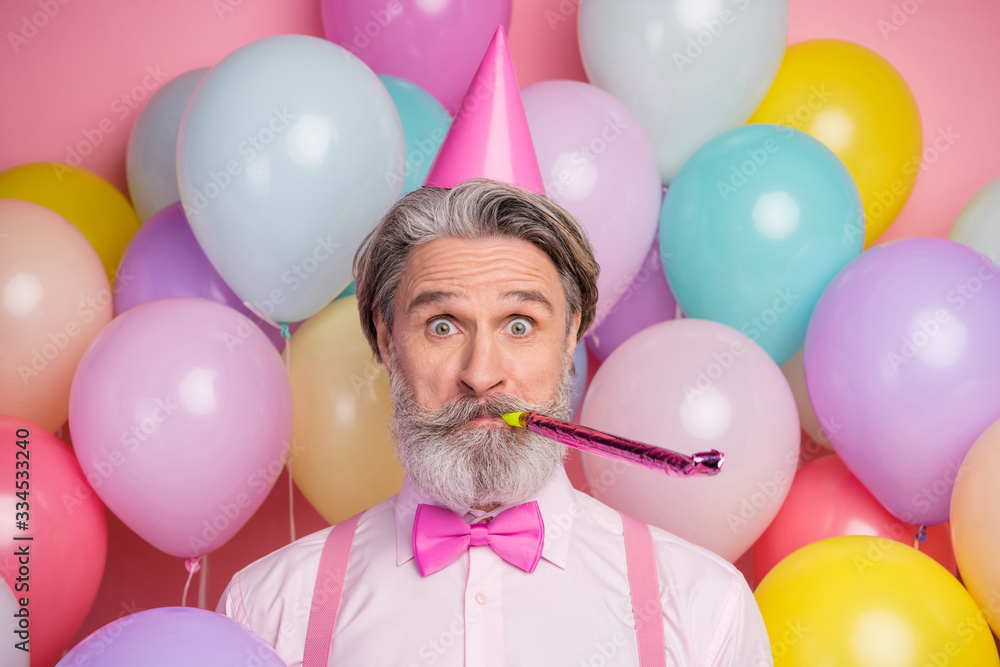 Close-up portrait of his he nice attractive cheerful funky grey-haired mature man having fun blowing festal whistle among colorful air balls isolated over pink pastel color background - obrazy, fototapety, plakaty 