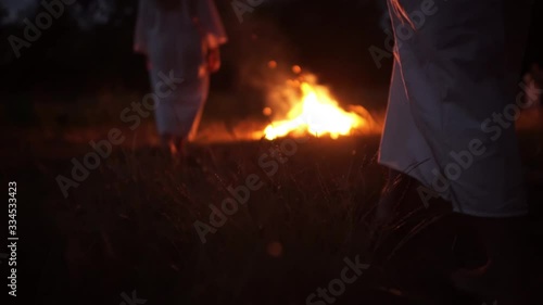 Girls in long white shirts barefoot walk across the grass to the fire, strange gathering, sect photo