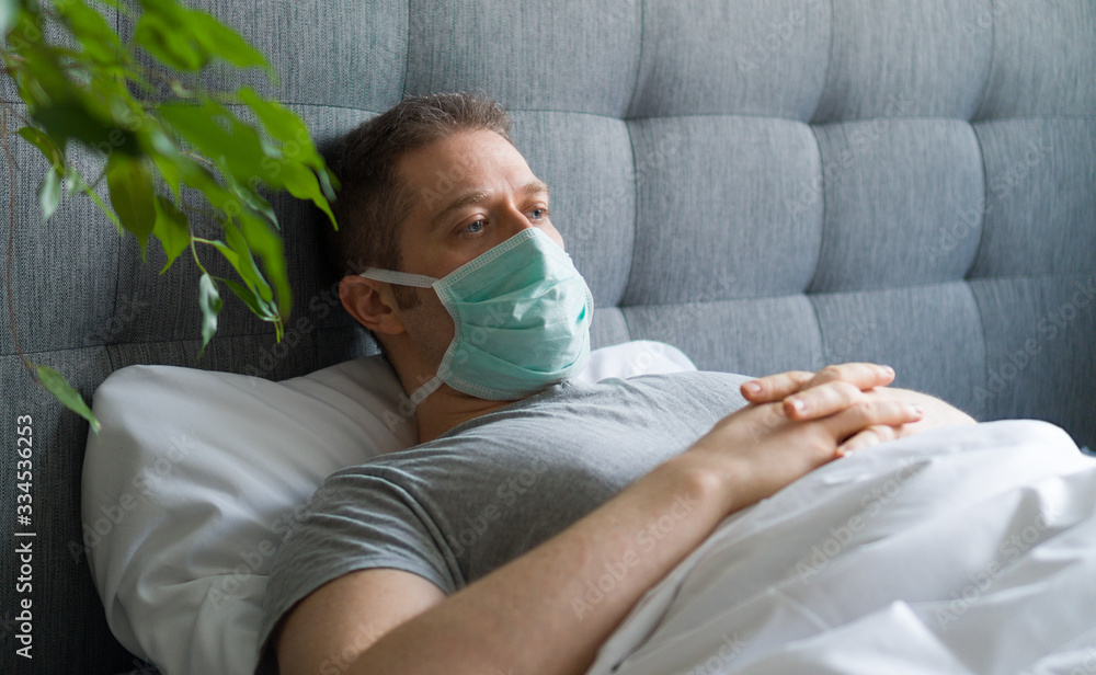 Sick man with medical mask lying in bed. Coronavirus quarantine concept.