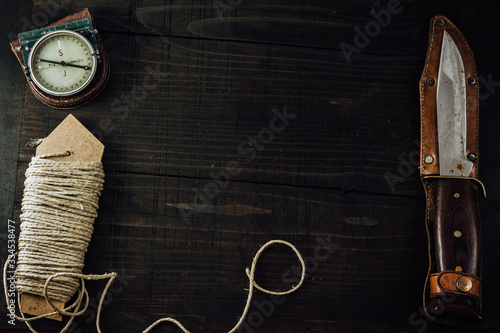 Old rusty hunting bushcraft knife, military compass and a linen rope on the wooden table. Leather cases, copy space, top view, survival concept. photo