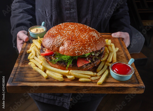 Young man holds a huge burger on a serving board