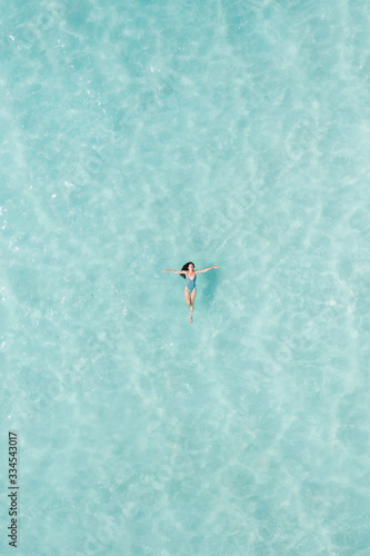 View from a drone of a girl floating on a blue lagoon at sunset