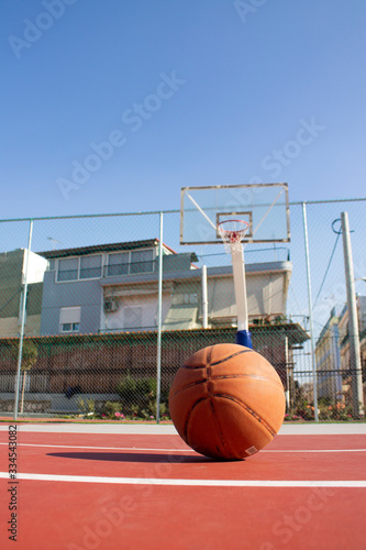 Used basketball in the foreground lies on a basketball court and a basketball basket with a blurred background