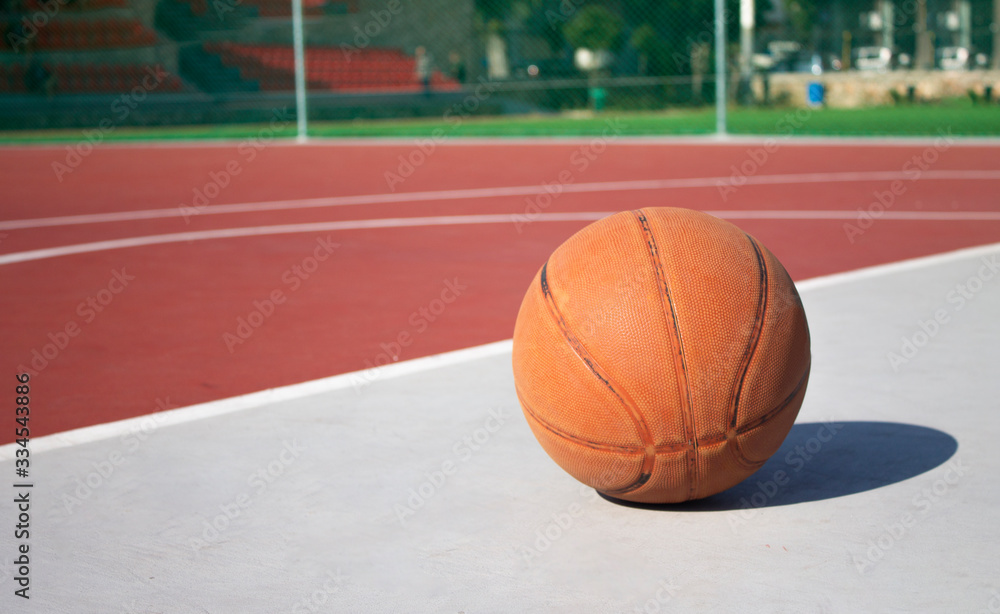Used basketball in the foreground lies on an empty basketball court with a blurred background
