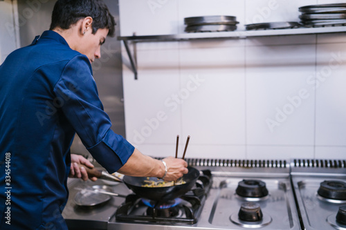 Young Chef preparing noodles with chopsticks in a wok a kitchen in a modern restaurant