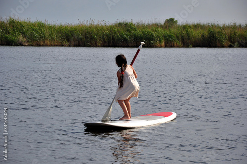 The woman on the board with a paddle floating on a calm sea sup.