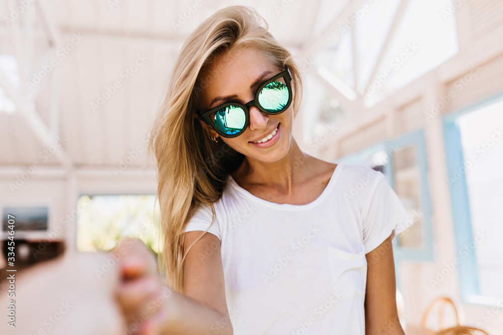 Happy white woman with suntan enjoying photoshoot in cafeteria. Indoor portrait of cute caucasian female model with beautiful blonde hair Happy white woman with suntan enjoying photoshoot in cafeteria. Indoor portrait of cute caucasian female model with beautiful blonde hair