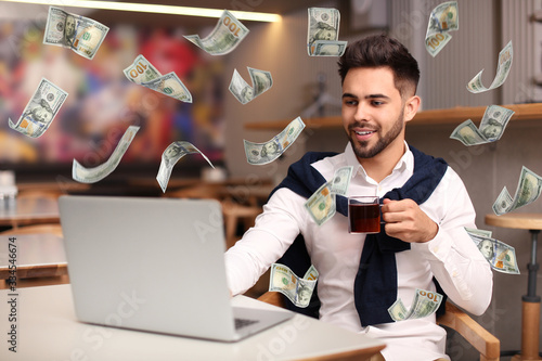 Cuadro en lienzo Man with modern laptop and flying dollar banknotes at table indoors