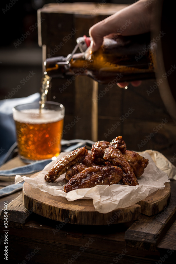 beer pouring into glass and fried chicken wings with sesame seeds on wooden background beer pouring into glass and fried chicken wings with sesame seeds on wooden background