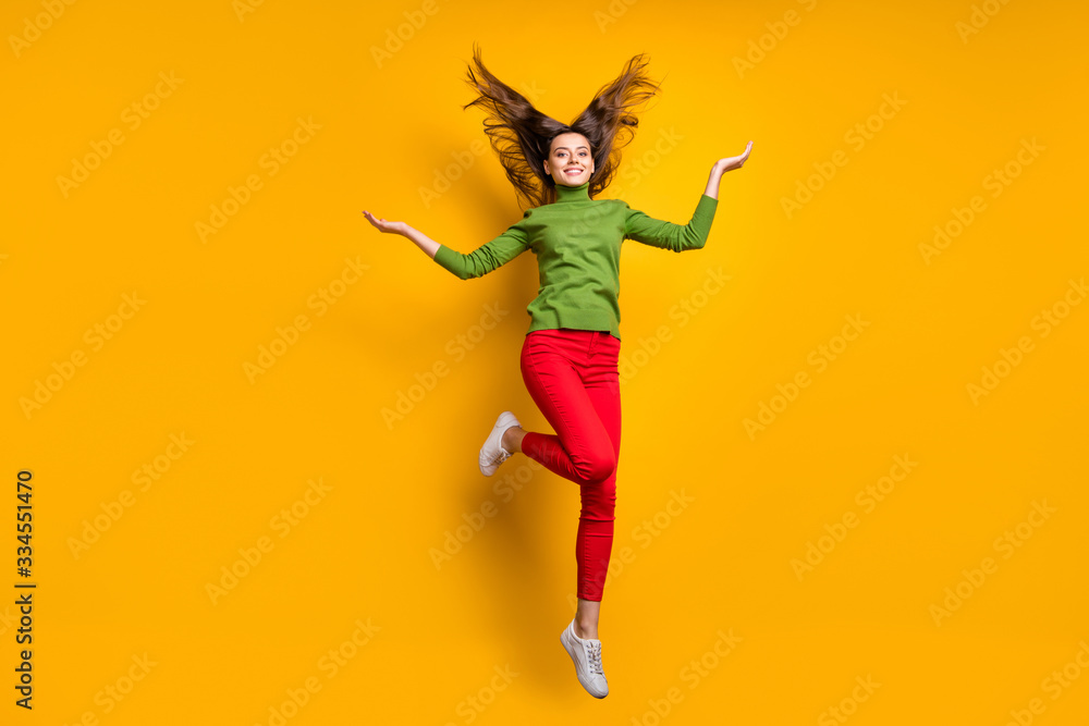 Full body photo of funky pretty lady jumping high throwing hairdo air feel freedom in veins wear casual green jumper red pants isolated yellow color background Full body photo of funky pretty lady jumping high throwing hairdo air feel freedom in veins wear casual green jumper red pants isolated yellow color background
