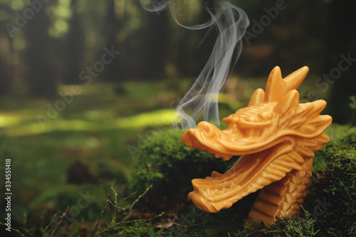 traditional golden chinese dragon sculpture with smoke curling frome nostrils stands in rich green forest scenery with blurred background