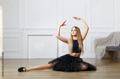 Young girl - ballet dancer in black tutu doing exercises and practice stretching leg up in studio