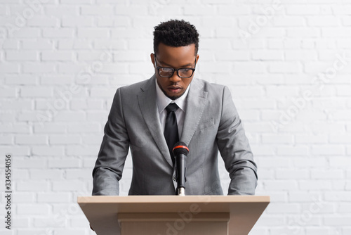 serious african american business speaker on tribune with microphone in conference hall