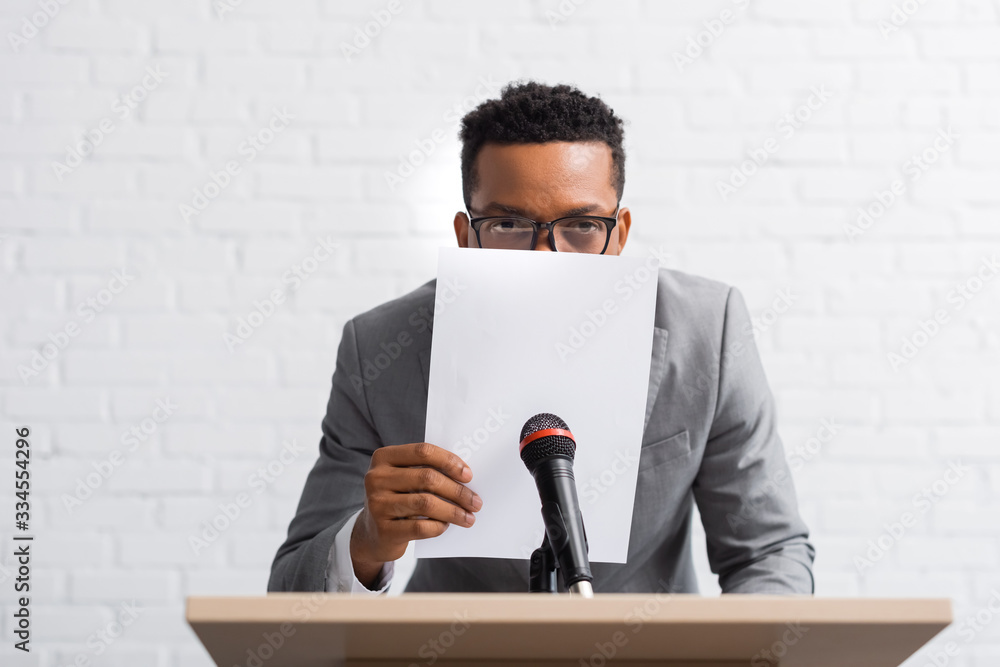 nervous african american speaker hiding behind paper during business conference nervous african american speaker hiding behind paper during business conference