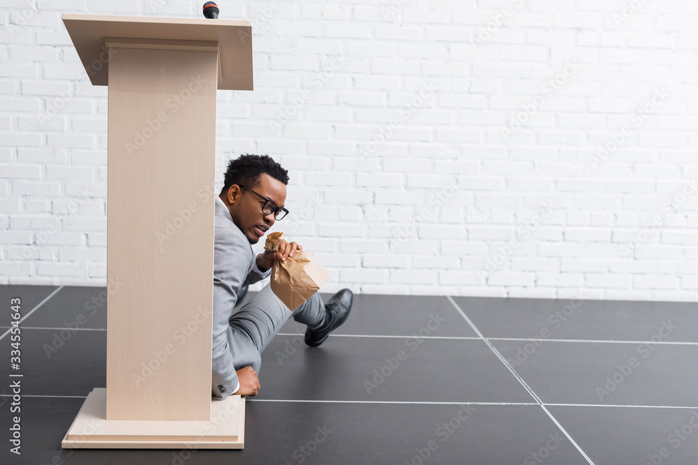 © LIGHTFIELD STUDIOS - scared african american speaker with paper bag having panic attack during business conference in office