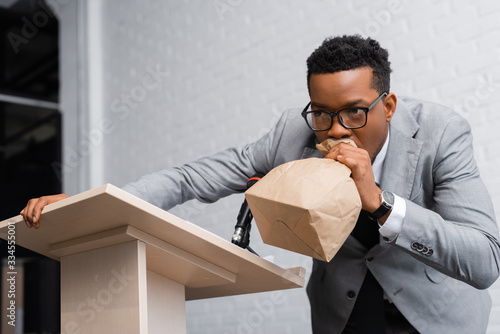 stressed african american speaker breathing with paper bag and having panic attack on business conference