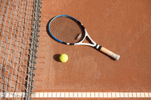 Tennis ball and racket on the ground on a clay tennis court next to the net and line © NomadCam