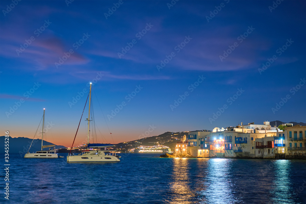 Sunset in Mykonos island, Greece with yachts in the harbor and colorful waterfront houses of Little Venice romantic spot on sunset and cruise ship illuminated in night. Mykonos townd, Greece