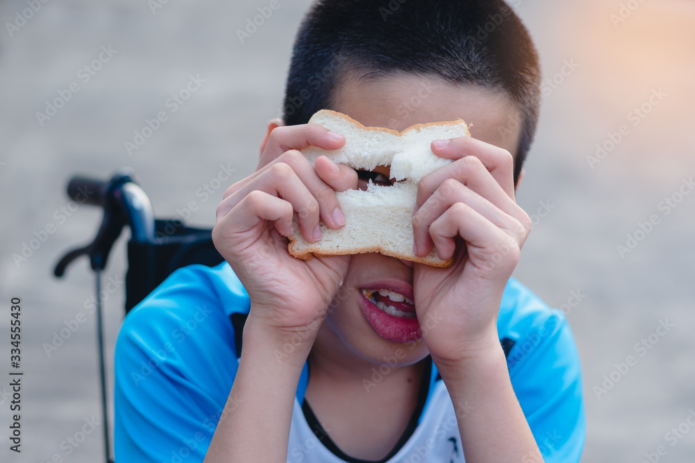 Asian disabled child on wheelchair eating bread by themselves,The skills to practice muscle development,Special children's lifestyle,Life in the education age,Happy disability kid concept. Asian disabled child on wheelchair eating bread by themselves,The skills to practice muscle development,Special children's lifestyle,Life in the education age,Happy disability kid concept.