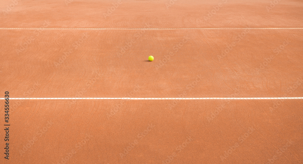 Abandoned tennis ball between horizontal lines on a clay tennis court. No match.