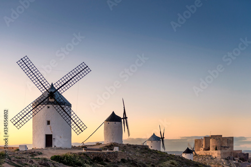 A group of old windmills located on a hill in the town of Consuegra (Spain) in front of a medieval castle, on the route of the Cervantes mills (Don Quixote), at sunset.