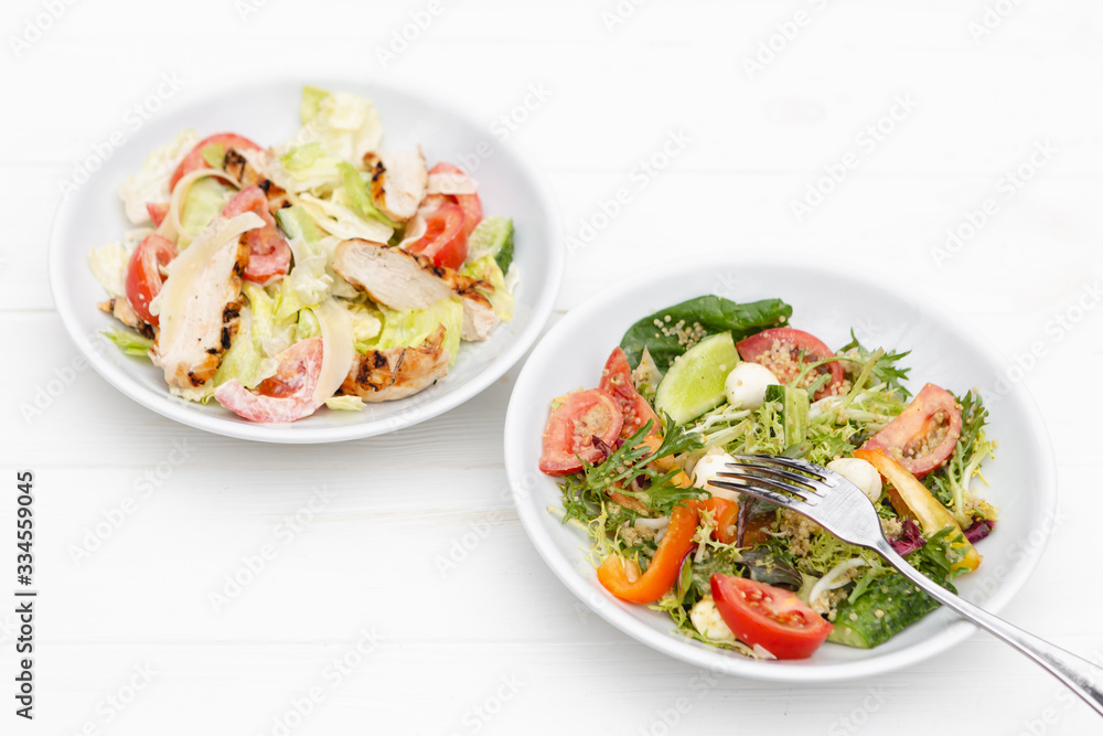 deep plates with fresh salad ingredients mixed with sauce placed on an attractive white table background. A place for a menu, banner or advertisement