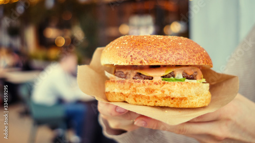 Girl holds burger in hands in a business center. Toned.