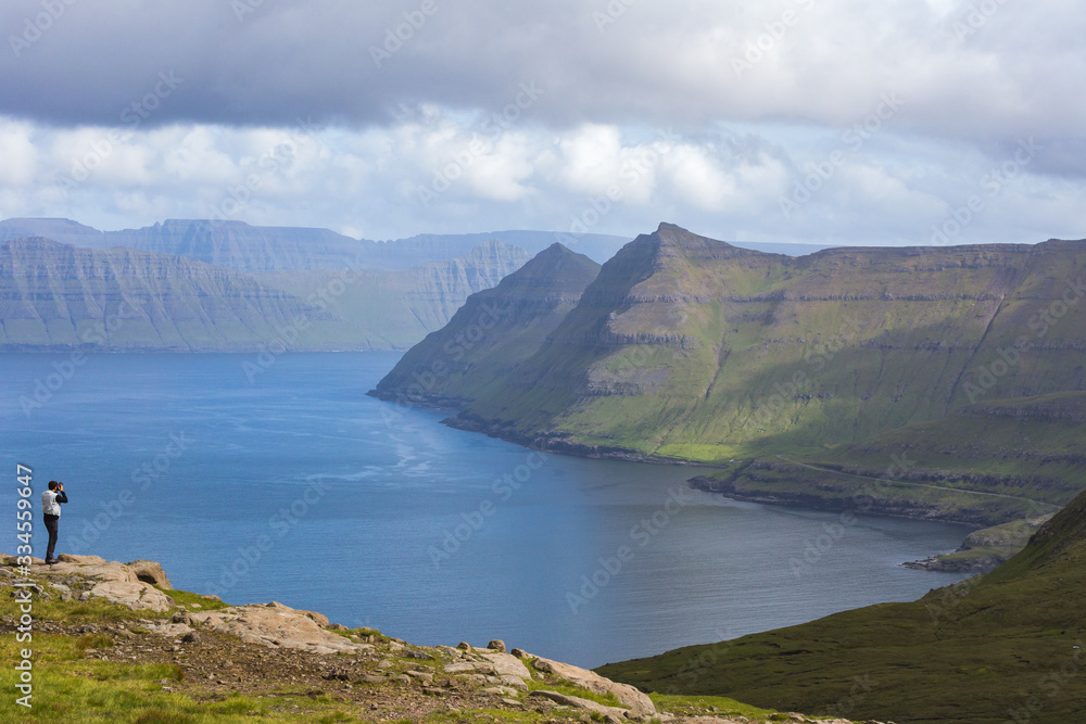 Hiker takes pictures of the fjords, Funningur, Eysturoy island, Faroe Islands, Denmark