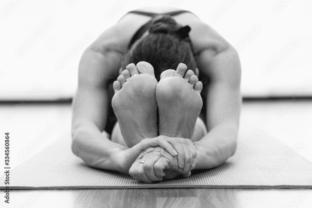 Hands of flexible woman on seated forward bend asana grabbing feet over