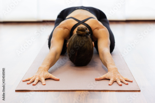 Yogi woman in balasana over bright white background. Hands of lady extended on pink mat and body resting on legs at studio. Healthy lifestyle, stretching exercise, wellness, yin yoga concepts