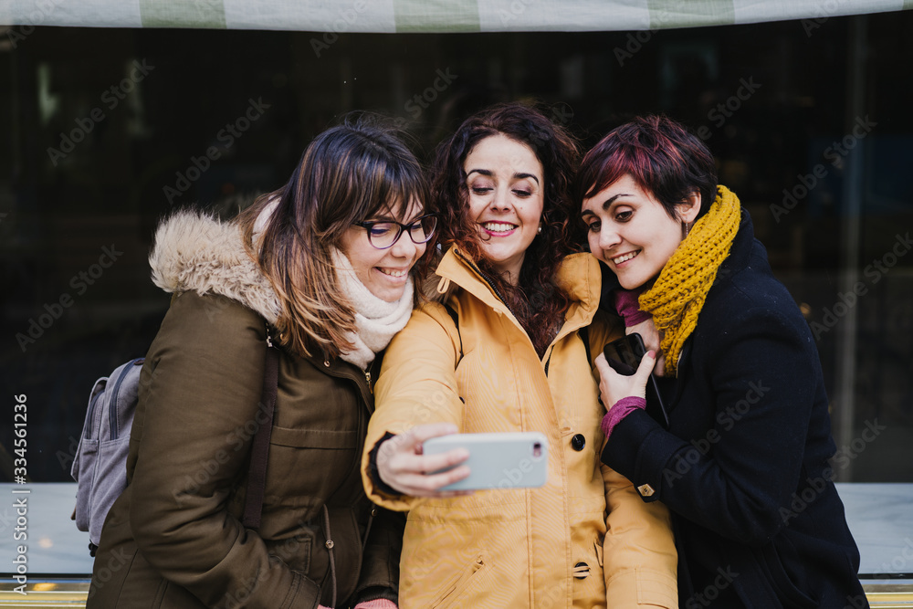 group of friends using mobile phone outdoors in the street. Happy women smiling. lifestyle and travel concept