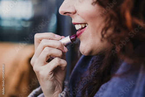 portrait of young beautiful woman using red lipstick outdoors in a terrace. Make up and lifestyle concept