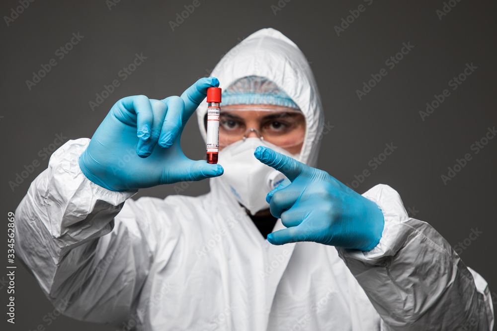 Coronavirus pandemia. The epidemic of the Chinese coronavirus virologist man in a protective suit, gloves, mask and glases examines the virus in a tube isolated on gray background Coronavirus pandemia. The epidemic of the Chinese coronavirus virologist man in a protective suit, gloves, mask and glases examines the virus in a tube isolated on gray background