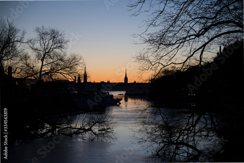 Morning view over the old town Gamla Stan in Stockholm with churches from the river passage Pålsundet in the district Södermalm, framed by trees in silhouette photo