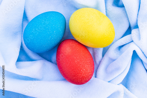 Three multicilired eggs over blue cloth, overhead view. Three bright Easter eggs lie on a crumpled blue cloth. Creative decoration on holiday photo