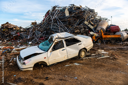 Tableau sur toile Broken and abandoned car next to a mountain of metal pieces in a junkyard