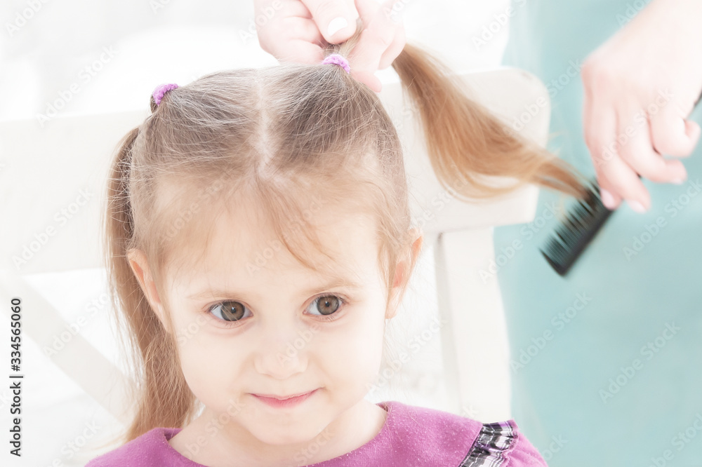 Naklejka premium hands of mother combing little smiling girl