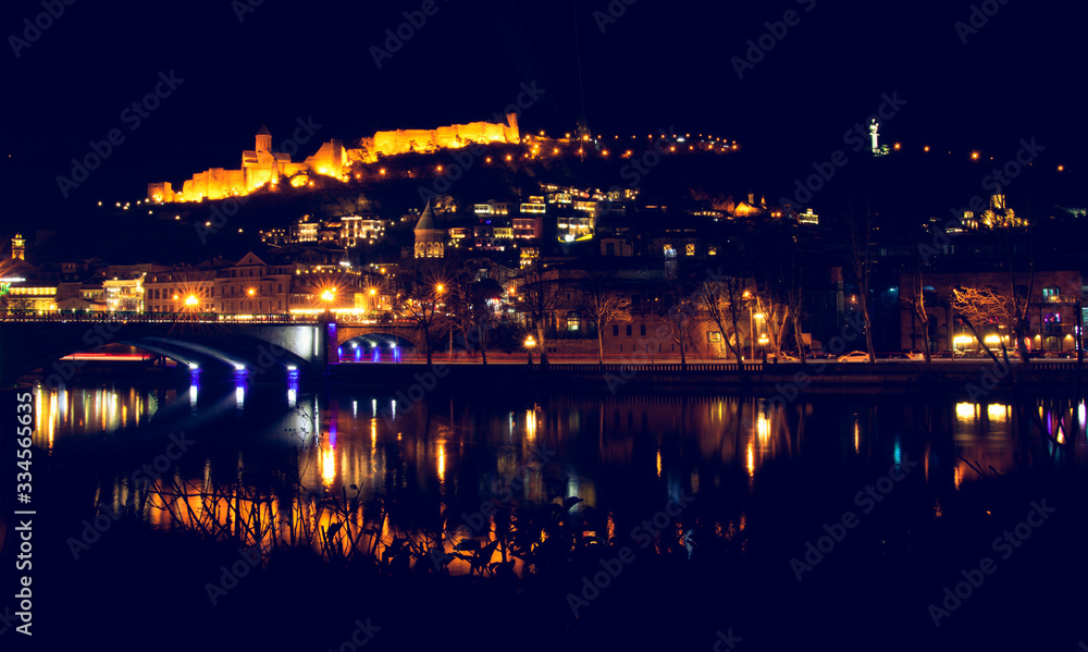 Night view of Mtkvari river and Metekhi bridge with old town in the background.Tbilis. Georgia.04.03.2020