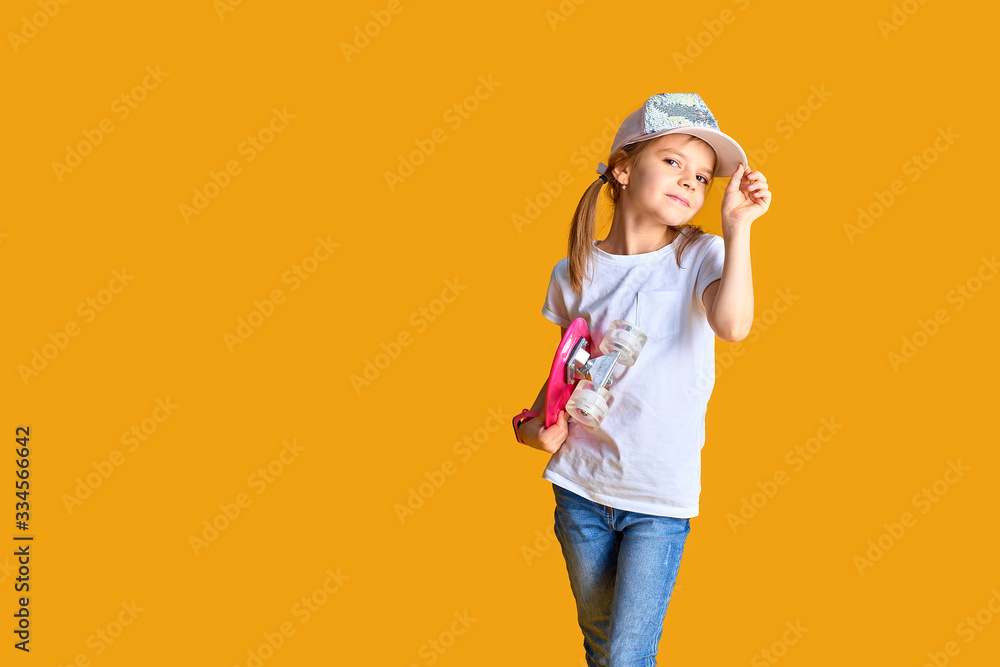 Stylish girl wearing white t-shirt, blue jeans and pink cap, holding skateboard over yellow background. Stylish girl wearing white t-shirt, blue jeans and pink cap, holding skateboard over yellow background.