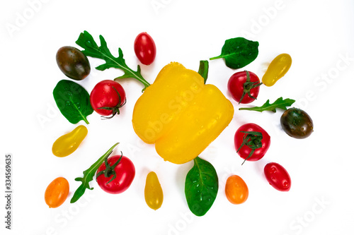 Cherry tomatoes of different colors, arugula leaves and basil around a bell yellow pepper. Fresh vegetables and herbs isolated on white