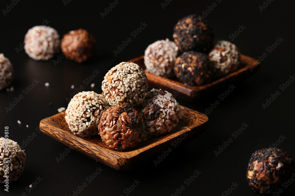 Healthy energy balls of nuts, oatmeals and dried fruit with coconut, flax and sesame seeds on wooden coconut plates on a black background, horizontal orientation Healthy energy balls of nuts, oatmeals and dried fruit with coconut, flax and sesame seeds on wooden coconut plates on a black background, horizontal orientation