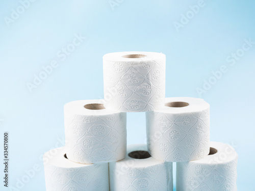Stack of white toilet paper rolls on blue abstract background. Personal hygiene supplies for restroom. Panic concept during coronavirus pandemic.
