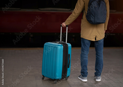 A young man with a blue suitcase is waiting for the train. Train station.