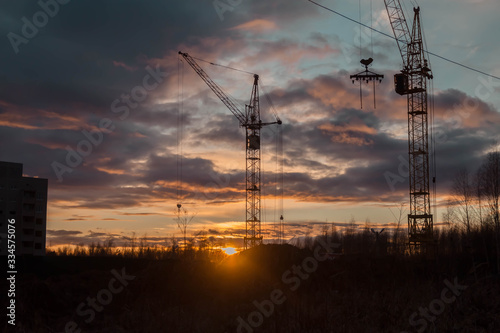 Cranes on the background of the sunset. House construction.