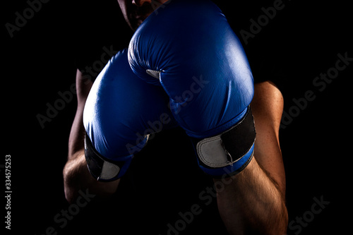 man stands in boxing stance, holds blue boxing gloves on his hands, dark background © Natallia