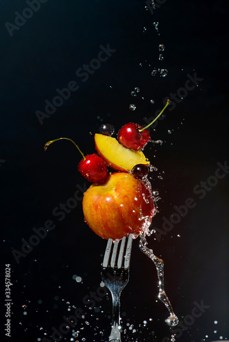  fresh fruits on a fork with flowing drops of water and spray on a black background