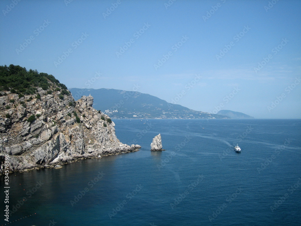 High rocky mountains rise above the blue water of a picturesque sea Bay, where a pleasure boat sails.